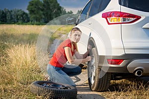 Beautiful woman changing car wheel on the rural road going through field