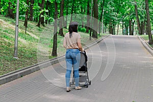 Beautiful woman with a child in a pram walks through a summer park.