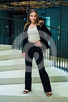 Beautiful woman in classic pants suit stands on a spiral staircase hand on hip domineering