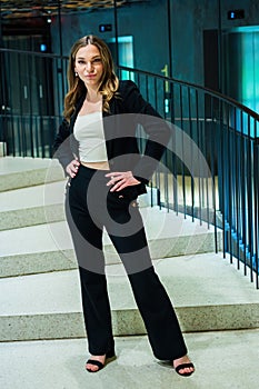 Beautiful woman in classic pants suit stands on a spiral staircase hands on hips