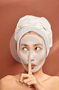 Beautiful woman with clay facial mask over orange background. Beauty treatment and spa concept