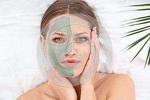 Beautiful woman with clay facial mask and tropical leaf on white fabric