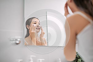 Beautiful woman cleaning her face with a foam treatment in bathroom