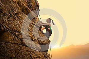 Beautiful Woman Climbing on the Rock at Foggy Sunset in the Mountains. Adventure and Extreme Sport Concept