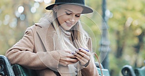 Beautiful woman in coat using smartphone relaxes on the bench in autumn park. Technology outdoors