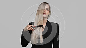 Beautiful woman combing her hair on gray background