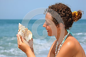 Beautiful woman considering seashell on seacoast