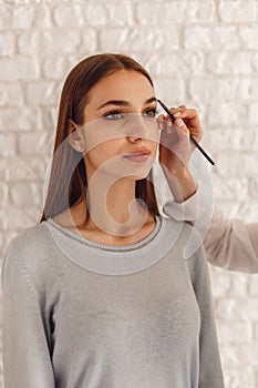 Beautiful woman and cosmetologist drawing a shape of eyebrows using cosmetic brush