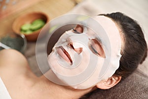 Beautiful woman with cotton mask sheet on face relaxing in spa salon