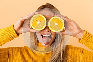 Beautiful woman covering eyes with citrus lemons posing isolated over yellow wall background