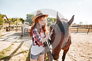 Beautiful woman cowgirl taking care of her horse on farm