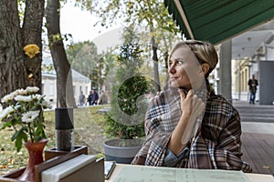 A beautiful woman in a cozy blanket at a table in a street cafe reads the menu. Relaxation in the city