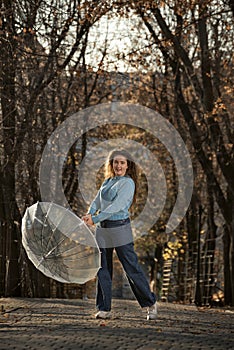 Beautiful woman with curly hair dance in alley of autumn park. Girl holds transparent umbrella and laughs