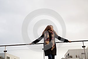 Beautiful woman with curly hair standing on terrace, enjoying cold autumn morning, sunny day. Speaking positive