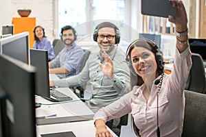 Beautiful woman customer support operator taking a selfie photo of her team colleagues in a call center.