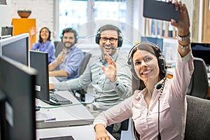 Beautiful woman customer support operator taking a selfie photo of her team colleagues in a call center