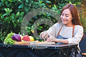 A beautiful woman cutting and chopping carrot by knife on wooden board with mixed vegetables in a tray
