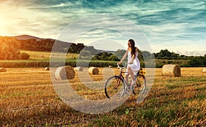 Beautiful woman cycling on an old red bike, in a wheat field