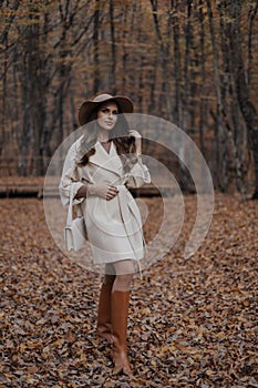 Beautiful woman with dark hair in elegant coat and hat walking in the autumn forest