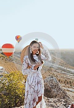 Beautiful woman with dark hair in elegant dress having picnic with fantastic view on valley with air balloons on background