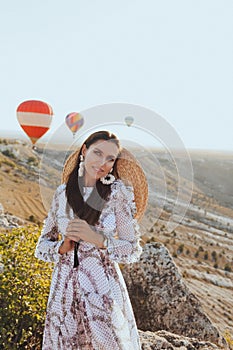 Beautiful woman with dark hair in elegant dress having picnic with fantastic view on valley with air balloons on background