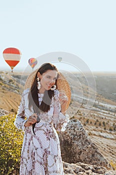 Beautiful woman with dark hair in elegant dress having picnic with fantastic view on valley with air balloons on background