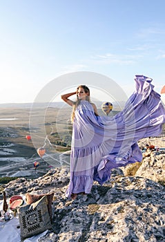 Beautiful woman with dark hair in elegant dress having picnic with fantastic view on valley with air balloons on background