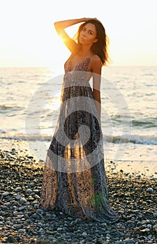 Beautiful woman with dark hair in elegant dress posing on sunset beach