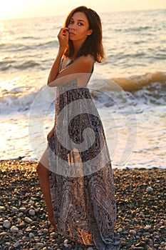 Beautiful woman with dark hair in elegant dress posing on sunset beach