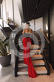 beautiful woman with dark hair in elegant red dress with accessories posing in luxurious hotel lobby