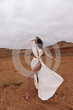 beautiful woman with dark hair in luxurious white dress with accessories posing in desert in Cyprus