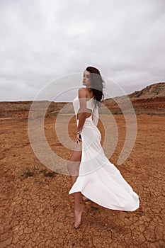 beautiful woman with dark hair in luxurious white dress with accessories posing in desert in Cyprus