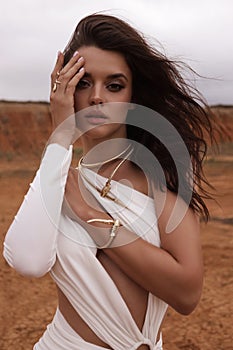 beautiful woman with dark hair in luxurious white dress with accessories posing in desert in Cyprus