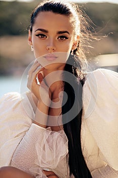 Beautiful woman with dark hair in luxurious white dress posing in beautiful landscape with sea view