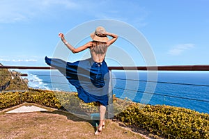 Beautiful woman with dark long hair in elegant blue dress posing in the cliff with ocean view