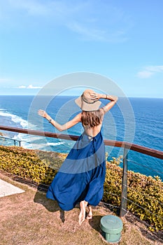 Beautiful woman with dark long hair in elegant blue dress posing in the cliff with ocean view