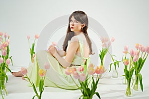 a beautiful woman in a delicate dress sits on the floor among bouquets of tulips