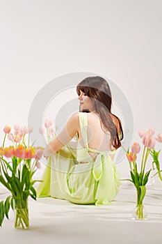 a beautiful woman in a delicate dress sits on the floor among bouquets of tulips