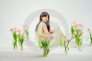 a beautiful woman in a delicate dress sits on the floor among bouquets of tulips