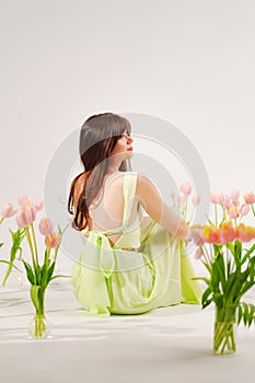 a beautiful woman in a delicate dress sits on the floor among bouquets of tulips