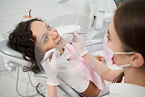 Beautiful woman in dentist`s chair during dental check-up in dentistry clinic on blurred foreground of dental hygienist holding