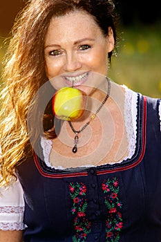 Beautiful woman in dirndl with an apple in her mouth