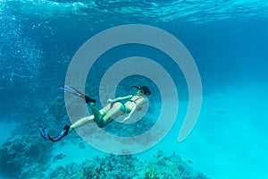 Beautiful woman diver swimming among the coral reef sea