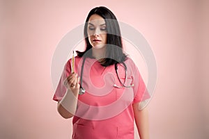 Beautiful woman doctor with stethoscope, wearing pink sctubs is looking at the thermometer