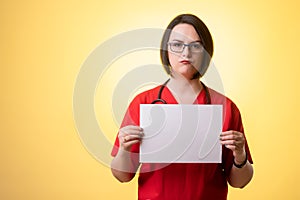 Beautiful woman doctor with stethoscope, wearing red scrubs holding a white paper