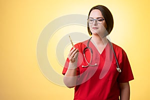 Beautiful woman doctor with stethoscope, wearing red scrubs is looking at the thermometer