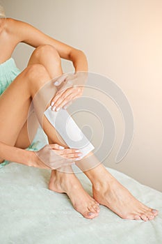 Beautiful woman doing depilation for her legs with waxing strip