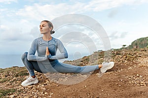 Beautiful woman doing yoga on a cliff, behind an amazing view in the ocean