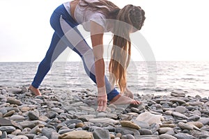 Beautiful woman is doing yoga on stone bach with sea view at sunset.