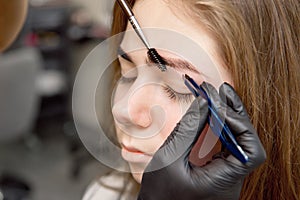 Beautiful woman drawing a shape of eyebrows using cosmetic brush. Make up artist applying make up to a model.